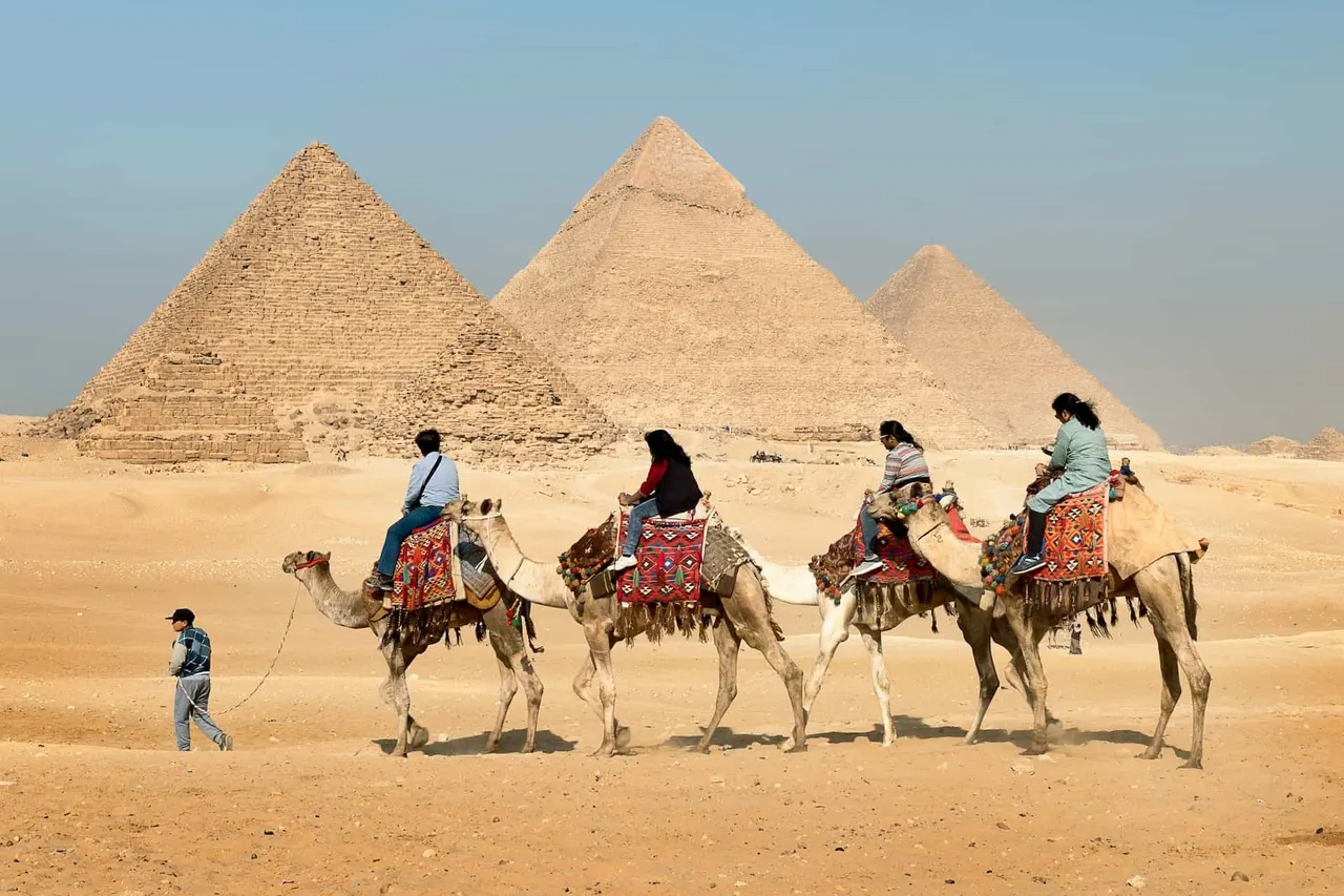 four-people-riding-on-camels-across-the-pyramids.jpg