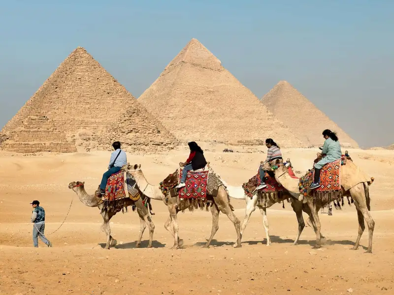 four-people-riding-on-camels-across-the-pyramids.jpg